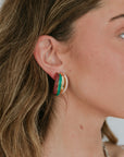 Close-up of a person wearing colorful hoop earrings with a neutral background