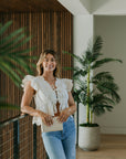 Woman in a white blouse and blue jeans holding Marissa Evening Bag standing indoors with plants in the background