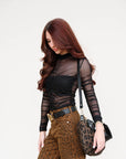 Woman wearing a sheer black top and leopard print pants holding a matching bag.