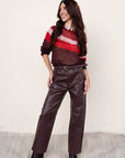 Woman wearing a red and brown striped sweater with leather pants against a white background
