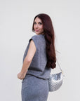 Woman in a gray outfit holding a silver handbag against a white background
