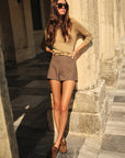Woman in beige sweater and shorts standing on stone steps outdoors