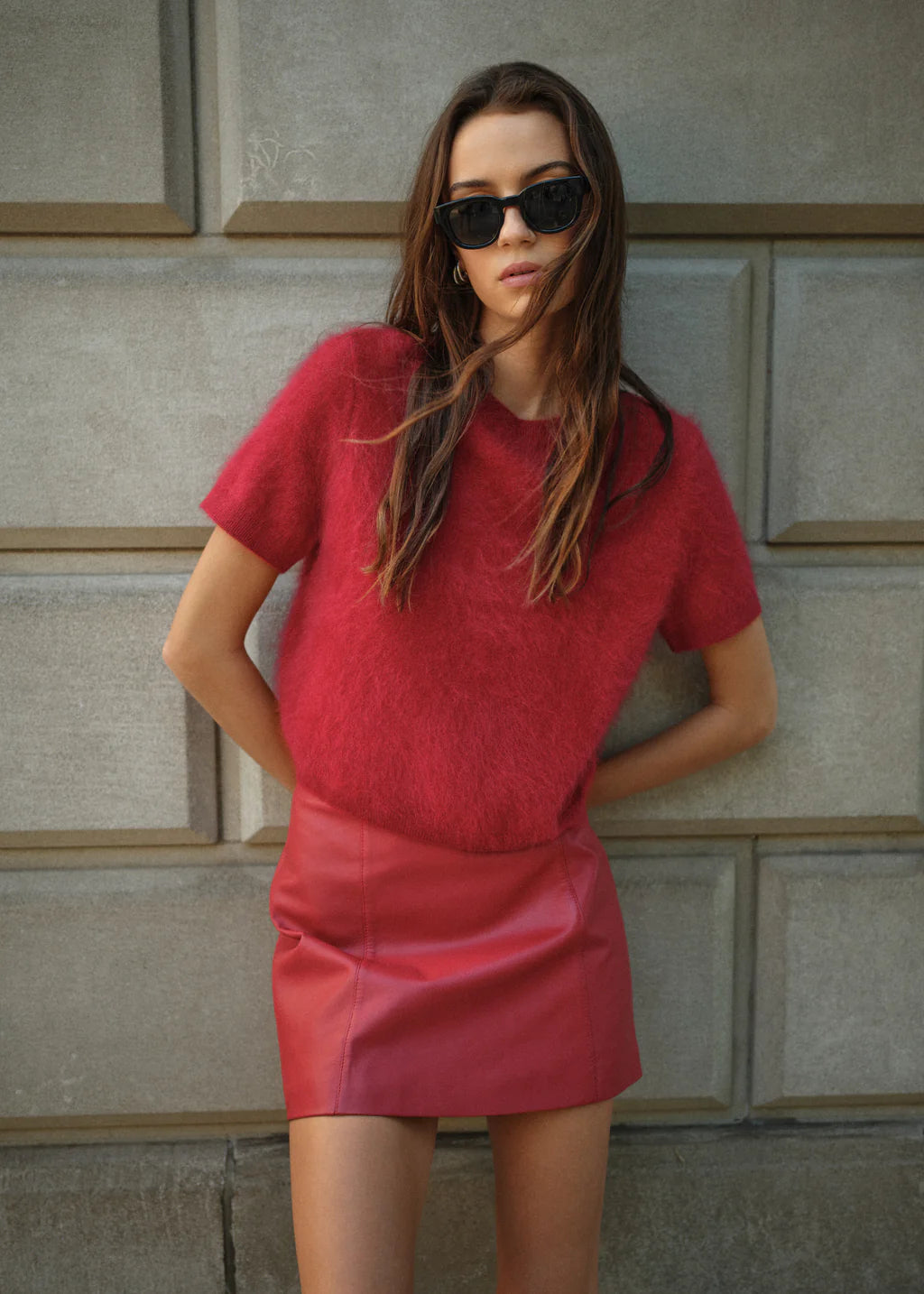 Woman wearing a red dress and sunglasses against a textured wall.