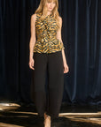 Woman wearing a sleeveless tiger print top and black pants on a runway with a dark curtain background.