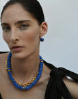 Woman wearing a blue beaded necklace and matching earrings against a plain background