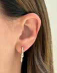 Close-up of an ear wearing a diamond hoop earring with a neutral background