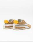 Pair of tan sneakers with yellow accents on a white background, back view