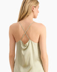 Woman wearing a light green satin tank top with thin straps on a white background