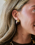 A close-up side profile of a woman wearing a dark brown and gold teardrop-shaped stud earring.