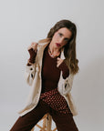 Woman posing in a stylish outfit with a beige jacket and brown pants against a plain background