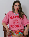 Woman wearing a pink 'Marina Piccola' shirt sitting on a chair.