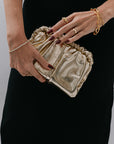 Gold clutch held by a hand with red nail polish against a black background