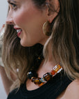 Woman wearing gold hoop earrings and a colorful beaded necklace.