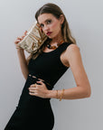 Woman in a black dress and Desert Mirage Collar Necklace holding a gold clutch against a plain background