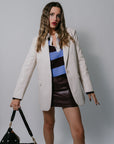 Woman wearing a beige blazer over a striped top and leather skirt, holding a black handbag against a plain background.