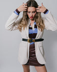 Woman wearing a beige blazer over a colorful top and brown leather skirt on a plain background