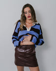 Woman wearing a colorful sweater and brown leather skirt against a plain background