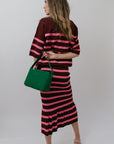 Woman wearing a striped set holding a green bag against a white background, back