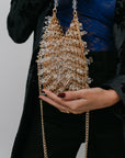 Person holding a sparkling handbag with a gold chain strap against a neutral background