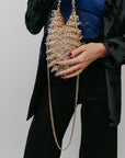 Person holding a decorative handbag with a gold chain against a neutral background