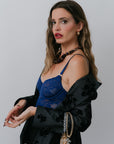 Woman wearing a blue lace top and black floral blazer against a plain background, side view