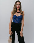 Woman wearing a blue lace top and black pants against a plain background