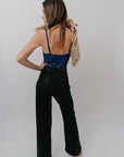 Woman wearing a blue top and black flared pants against a white background, back view