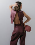 Woman in a two-piece outfit with a maroon top and maroon pants, holding a checkered clutch against a plain background. back view