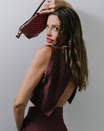 Woman in a burgundy set holding a checkered handbag against a plain background, back view