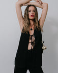Woman in a black outfit with lace-up details against a plain background