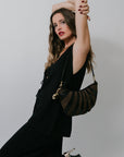 Woman in a black set holding a black and brown handbag against a plain background, side view