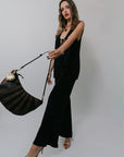 Woman in a Poppy Pant and tank holding a black handbag against a plain background