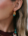 Close-up of a person wearing gold hoop earrings with turquoise stones.