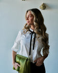 model wearing a white top with a black bow at the neck holding a large green tassel clutch