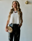 model wearing a statement necklace with a white tassel top and black bottoms holding a gold clutch