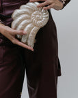 Person holding a decorative white shell-shaped clutch against a plain background