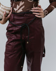 Person wearing a brown patterned top and maroon leather pants on a white background, close up