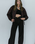 Woman wearing a brown jacket and dark brown pants against a white background