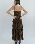 Woman wearing a brown tiered dress against a white background, back view