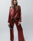 Woman wearing a burgundy satin blouse and pants against a white background
