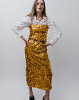Woman wearing a gold sequin dress over a white shirt on a plain background