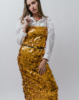 Woman wearing a gold sequin dress over a white shirt on a plain background