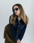 Woman wearing a denim jacket and sunglasses against a white background