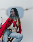 Woman in a red jacket and light blue jeans sitting on a chair with a white background