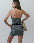 Woman wearing a strapless patterned dress holding a clutch against a plain background, back