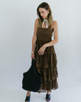 Woman wearing a brown dress holding a black bag against a white background