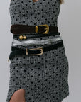 Person wearing a patterned dress with multiple belts and buckles on a gray background, close up