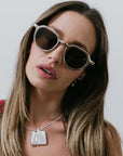 Woman wearing round sunglasses and silver necklace with a neutral background
