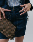Person wearing a denim skirt with a patterned bag and striped shirt on a plain background