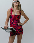 Woman in a red and black patterned set holding a book against a plain background